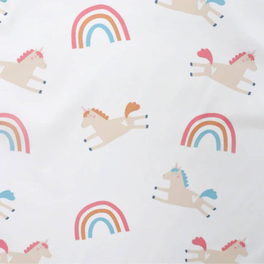 A close-up of a white fabric printed with pastel unicorns and colourful rainbows in pink, orange and blue tones on a soft weaning bib.