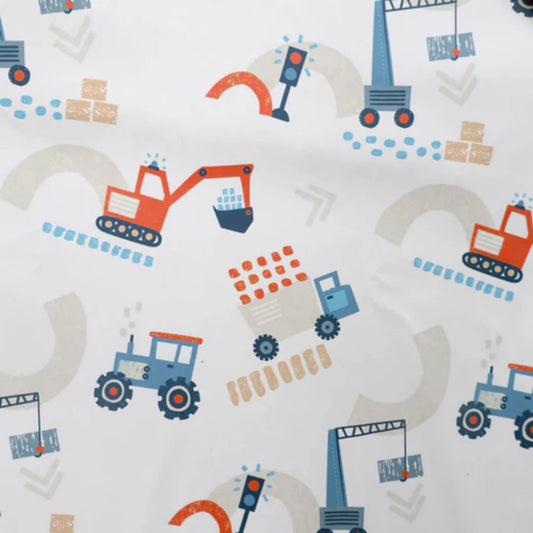 A close-up of a white fabric printed with orange diggers, blue tractors, cranes, trucks and construction-themed patterns in soft blue, orange and beige tones.