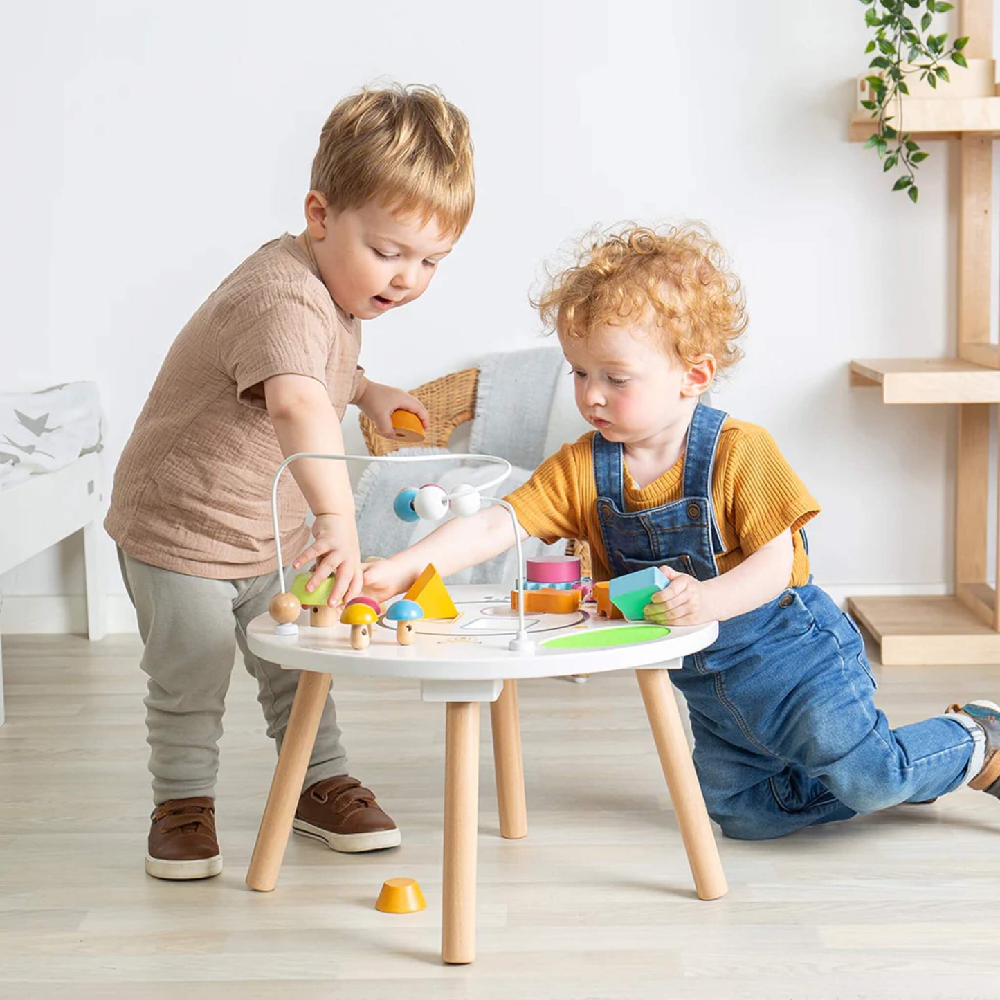 Toddlers exploring the activity table together, building social skills and fine motor control.