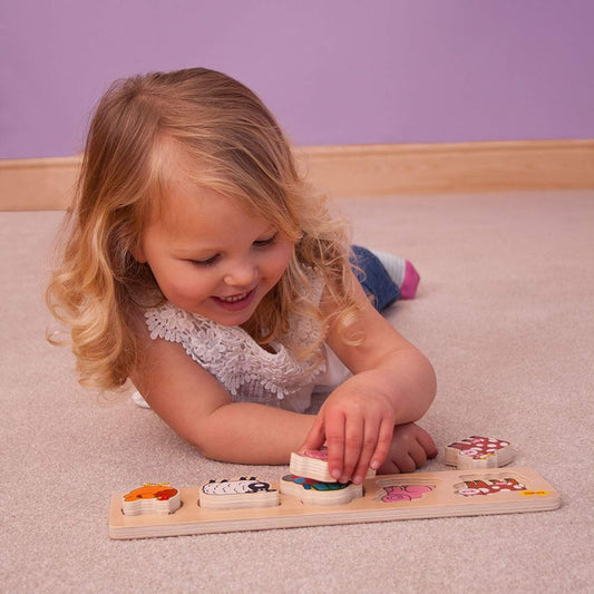 Smiling child playing with a wooden farm puzzle, carefully lifting a chunky piece from the board.