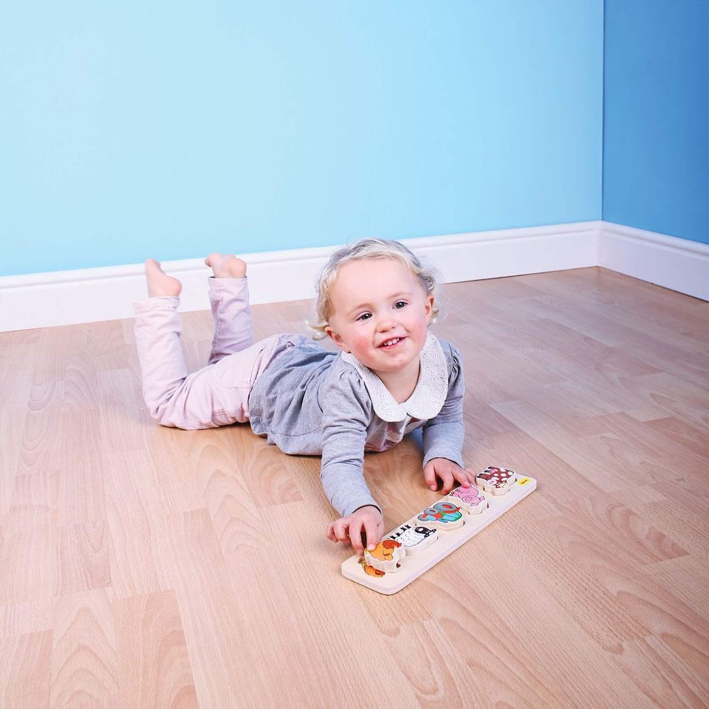 Happy child lying on the floor, exploring a wooden farm puzzle with colourful animal pieces.