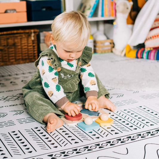 Toddler playing with the Bigjigs animal shape puzzle on a patterned playmat in a cosy room.
