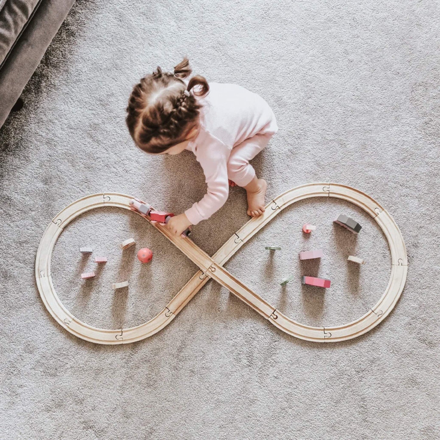 Overhead view of a child playing with the Bigjigs Toys Fairy Figure of Eight Train Set, arranging pastel houses and trees around the track.