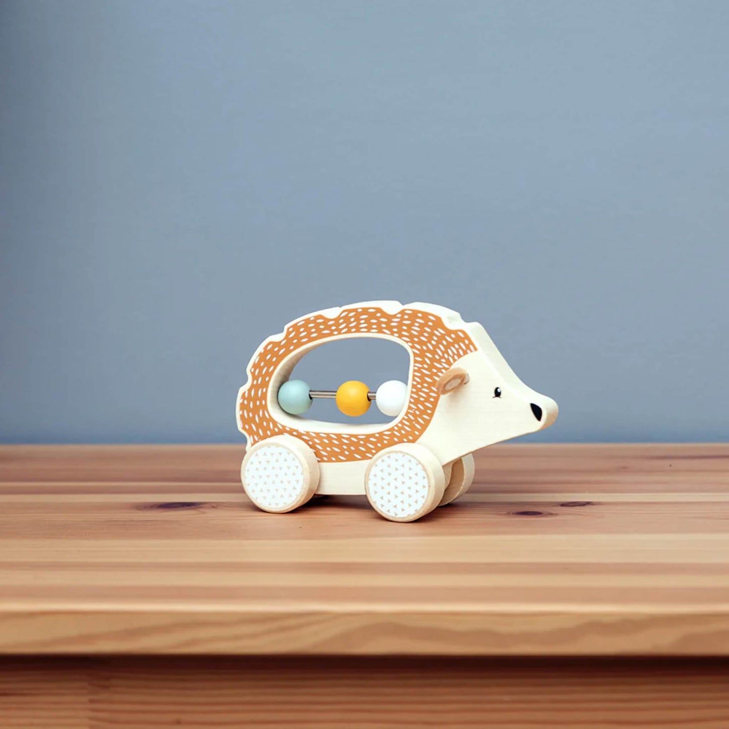 The Push Along Hedgehog toy positioned on a wooden surface with a soft grey-blue background.