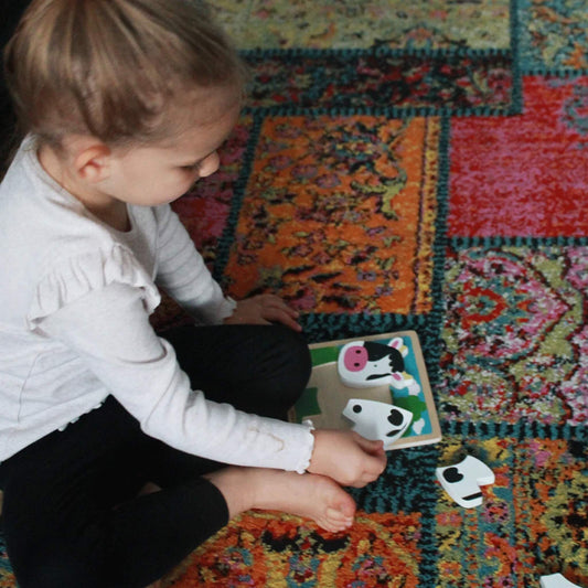 A toddler carefully placing chunky cow puzzle pieces on a sturdy wooden base, exploring shapes and colours.