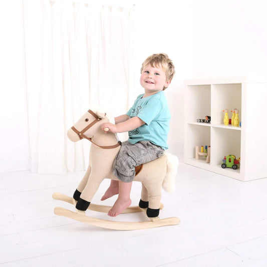 A smiling toddler riding the Bigjigs Toys Cord Rocking Horse indoors, holding the wooden handles confidently.