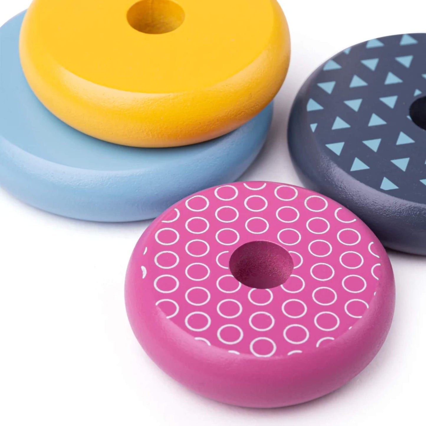 A selection of brightly painted stacking rings laid out flat, showing the mix of solid colours and geometric patterns.