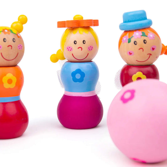 Close-up of three fairy skittles with the pink wooden ball in the foreground, showing painted flower details and cheerful facial expressions.