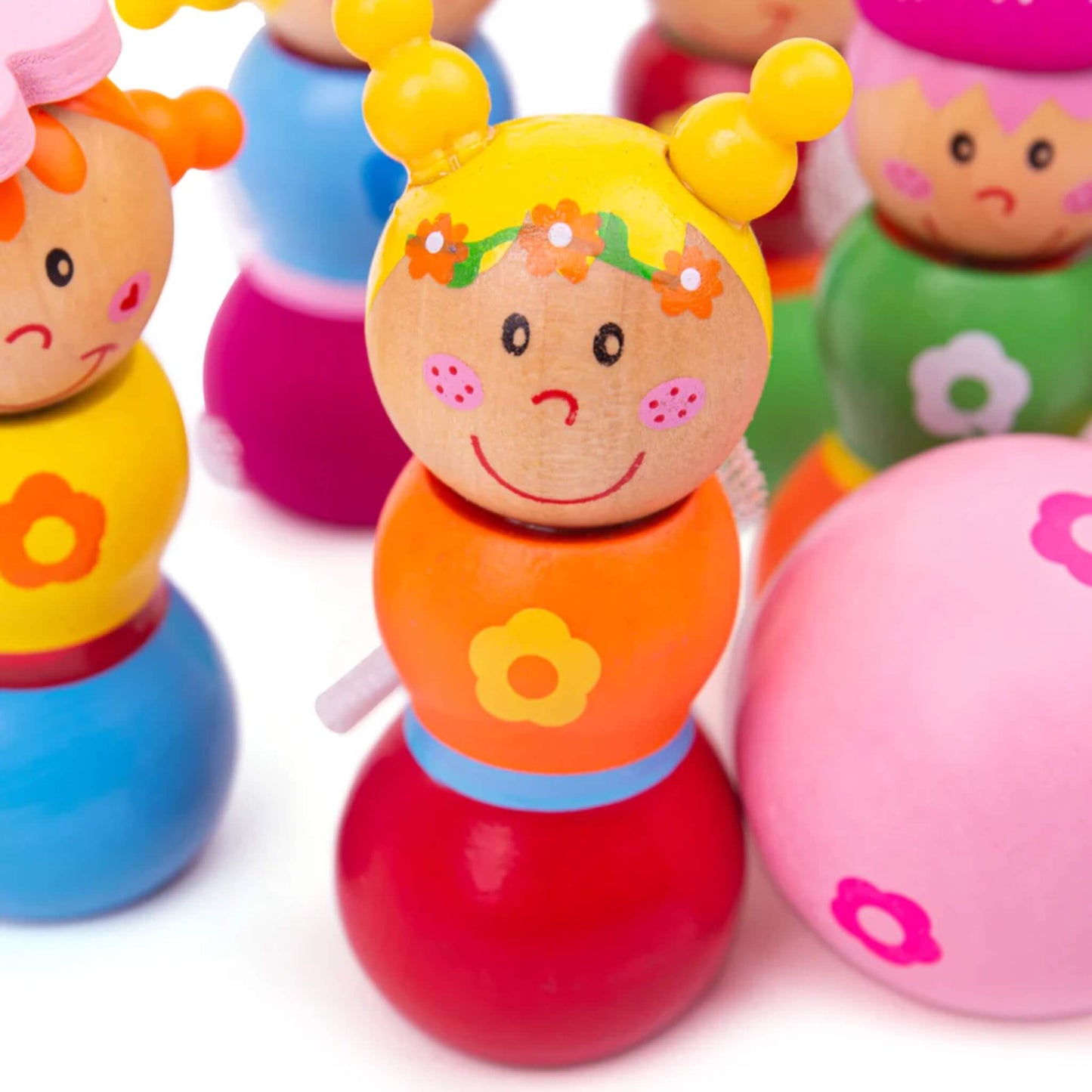 Detailed close-up of one fairy skittle with yellow hair and an orange dress, next to the pink ball, surrounded by other colourful fairies in the background.