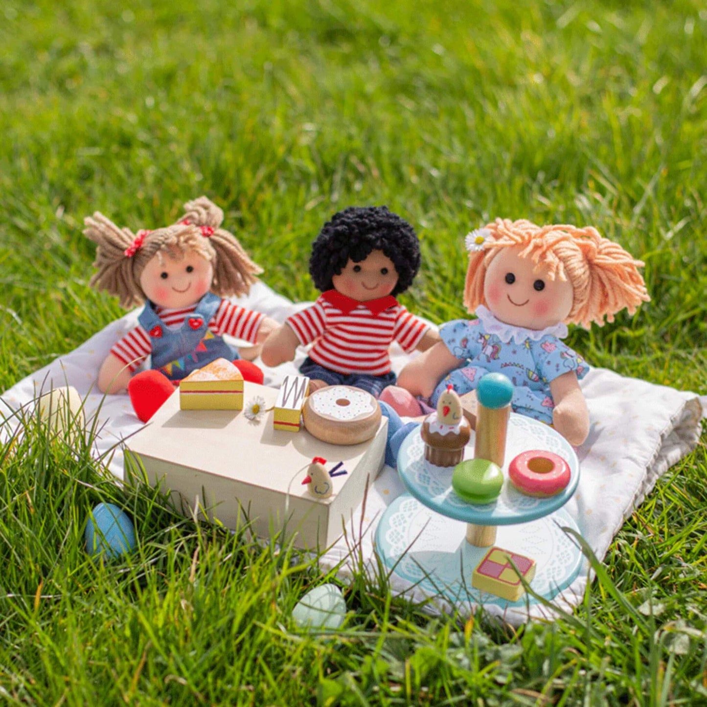 Olivia Doll enjoying a toy picnic on the grass with two other Bigjigs rag dolls and a wooden tea set.