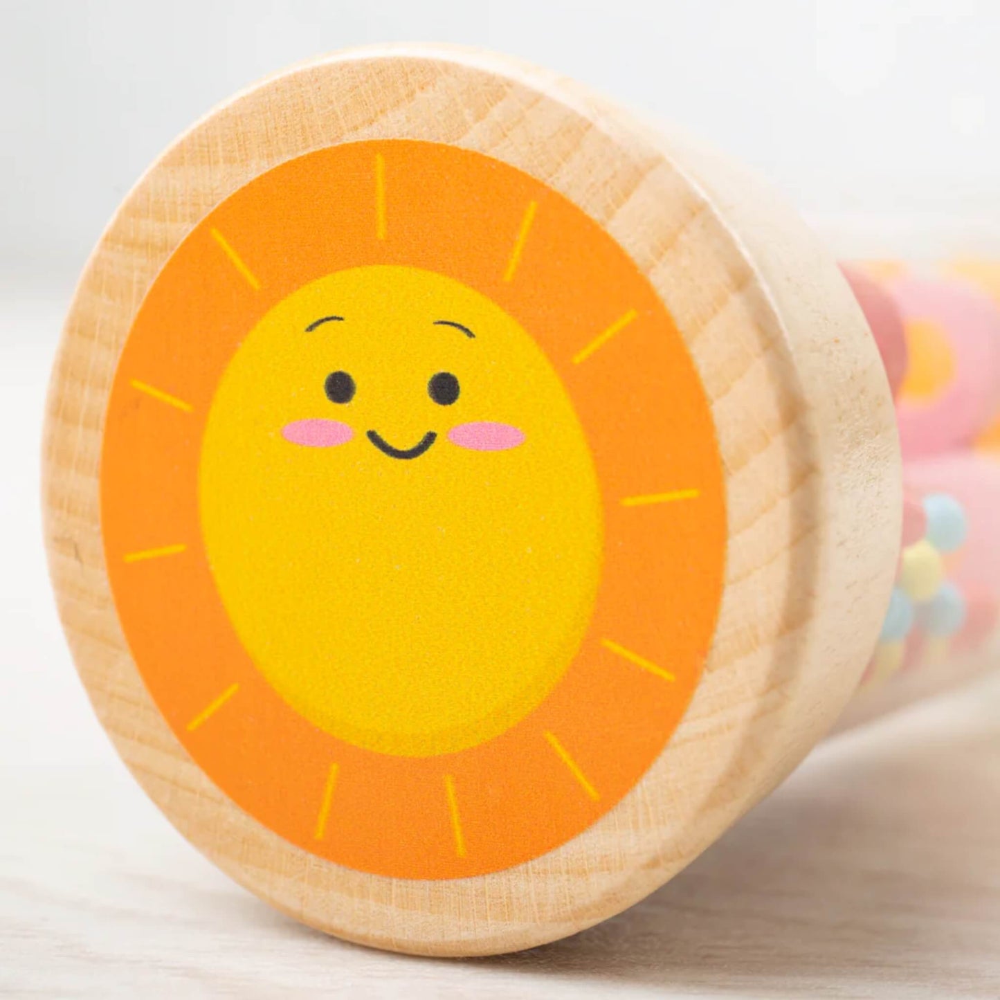 Close-up of the sun illustration on the wooden top of the Bigjigs Toys Rainmaker, showing a bright yellow sun with a smiling face and orange rays.