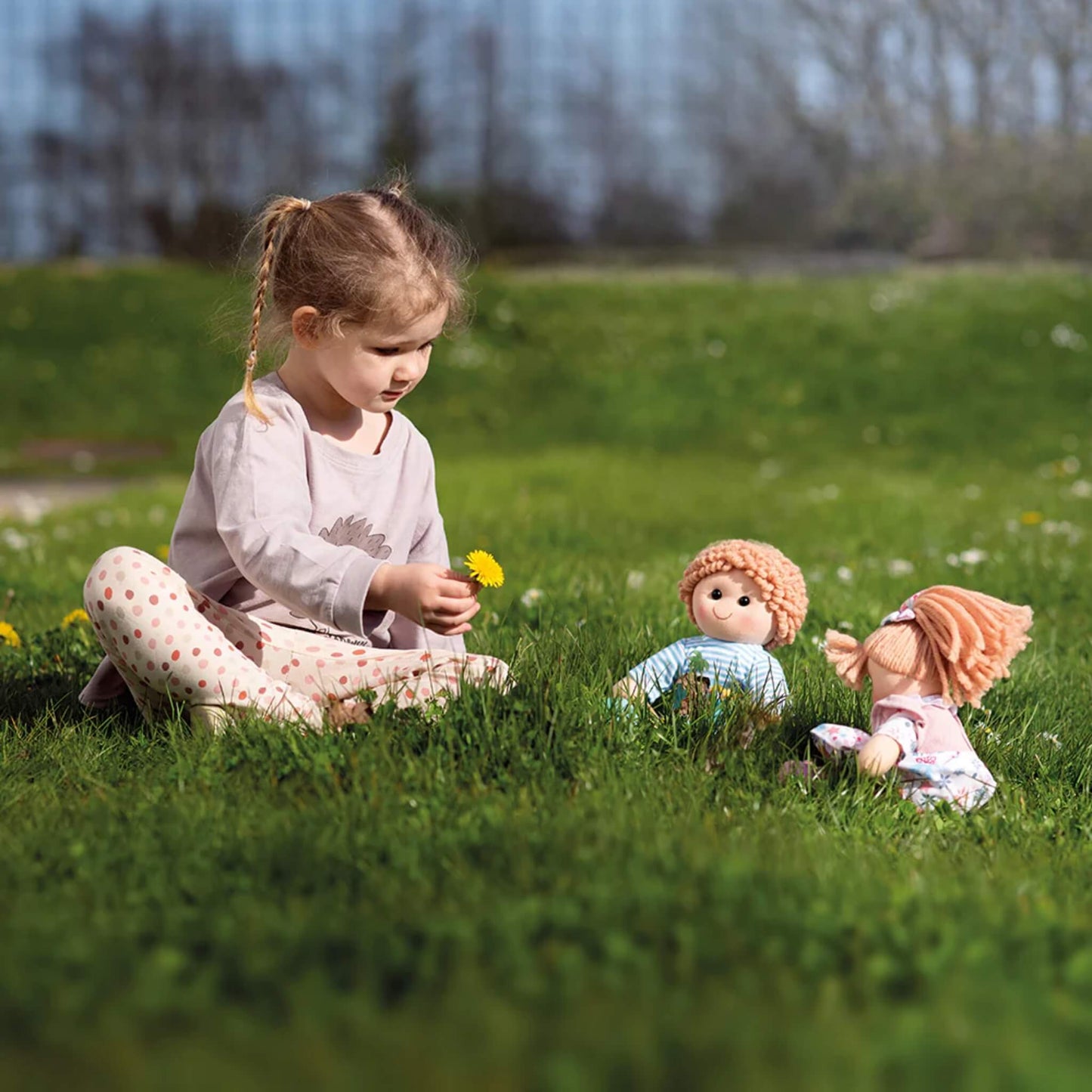 Child playing outdoors with two Bigjigs Toys ragdolls, including Shannon sitting in the grass.