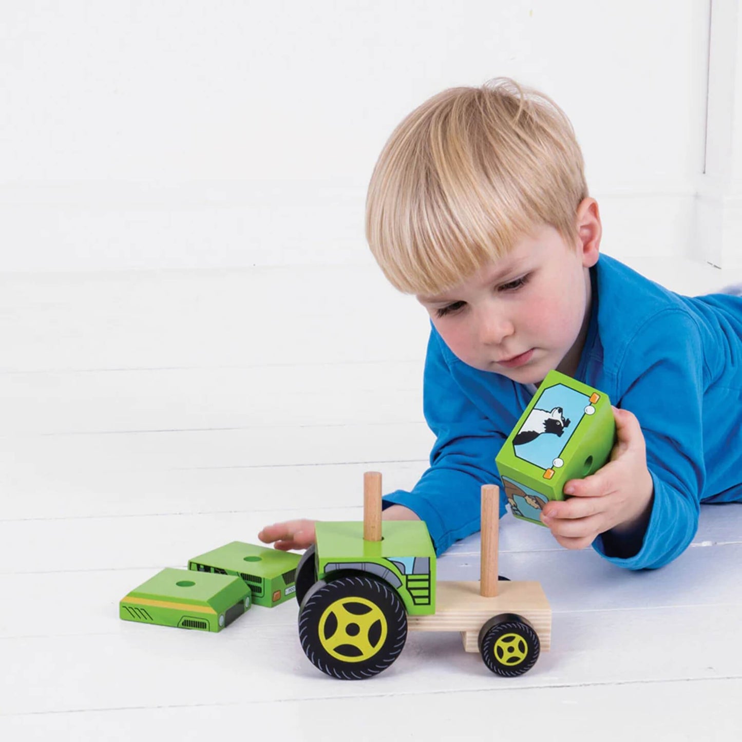A young child playing with the Bigjigs Toys Stacking Tractor, examining a wooden block while assembling the toy—ideal for hands-on, open-ended play.