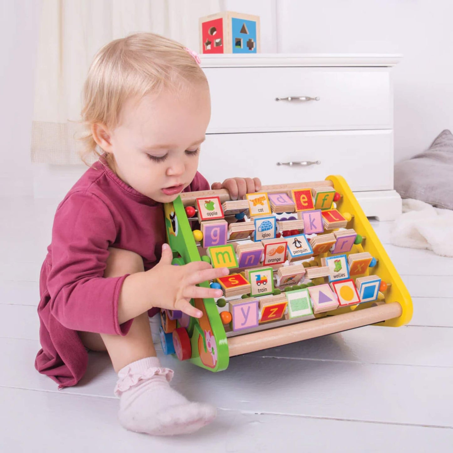 Toddler sitting on the floor playing with the alphabet side of the Bigjigs Toys Triangular Activity Centre.
