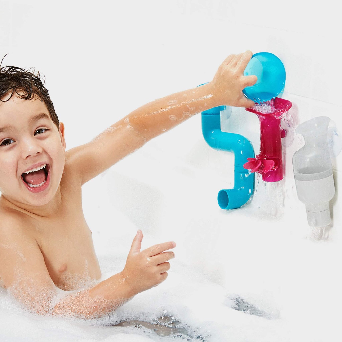 Smiling child splashing water into Boon pipes and cogs for bath time excitement.