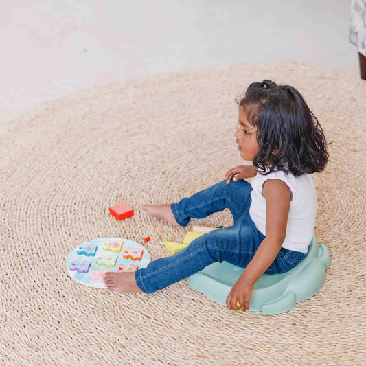 Child sitting on the Bumbo Elipad in Hemlock while playing with a puzzle on a woven rug.