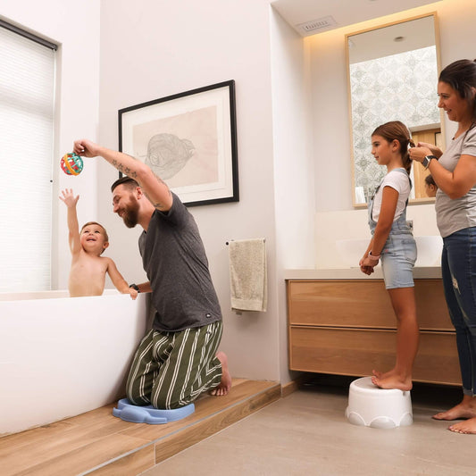 Adult using the Bumbo Elipad in Powder Blue while kneeling by the bath, playing with a toddler.