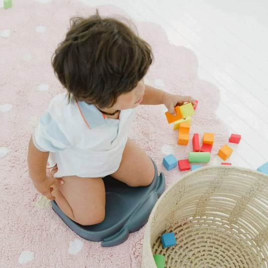 Child kneeling on the Bumbo Elipad in Slate Grey while playing with colourful blocks on a pink rug.