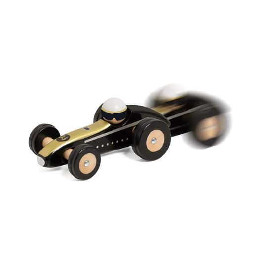 Motion blur image of a black and gold wooden Indianapolis toy car racing forward, capturing the sense of speed and movement.