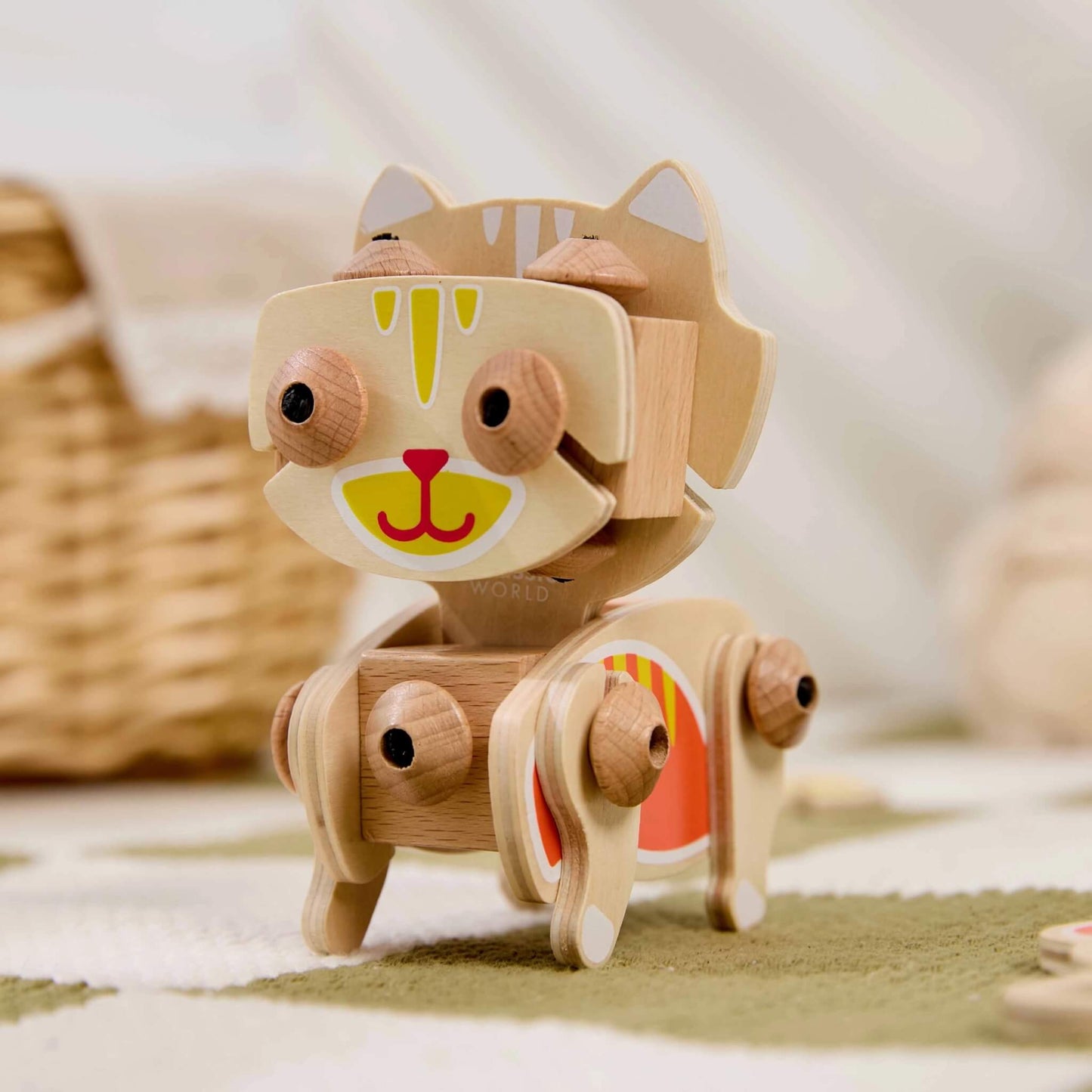 Wooden cat construction toy standing upright with flexible legs and body joints on a patterned mat in a softly styled play setting.