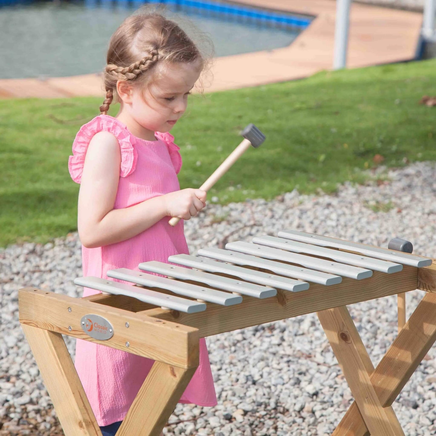 Close-up of a child using a mallet to play an outdoor metallophone, focusing on the keys and stand.