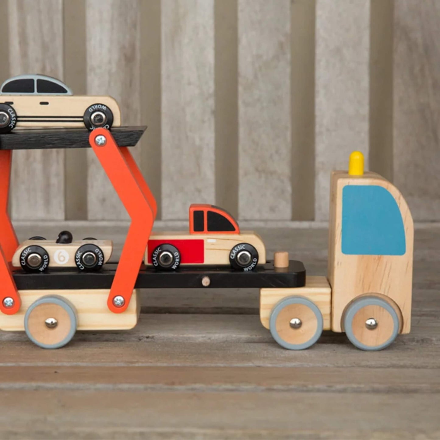 Close-up side view of the wooden vehicle carrier toy, showing the three small cars and the working lift ramp.