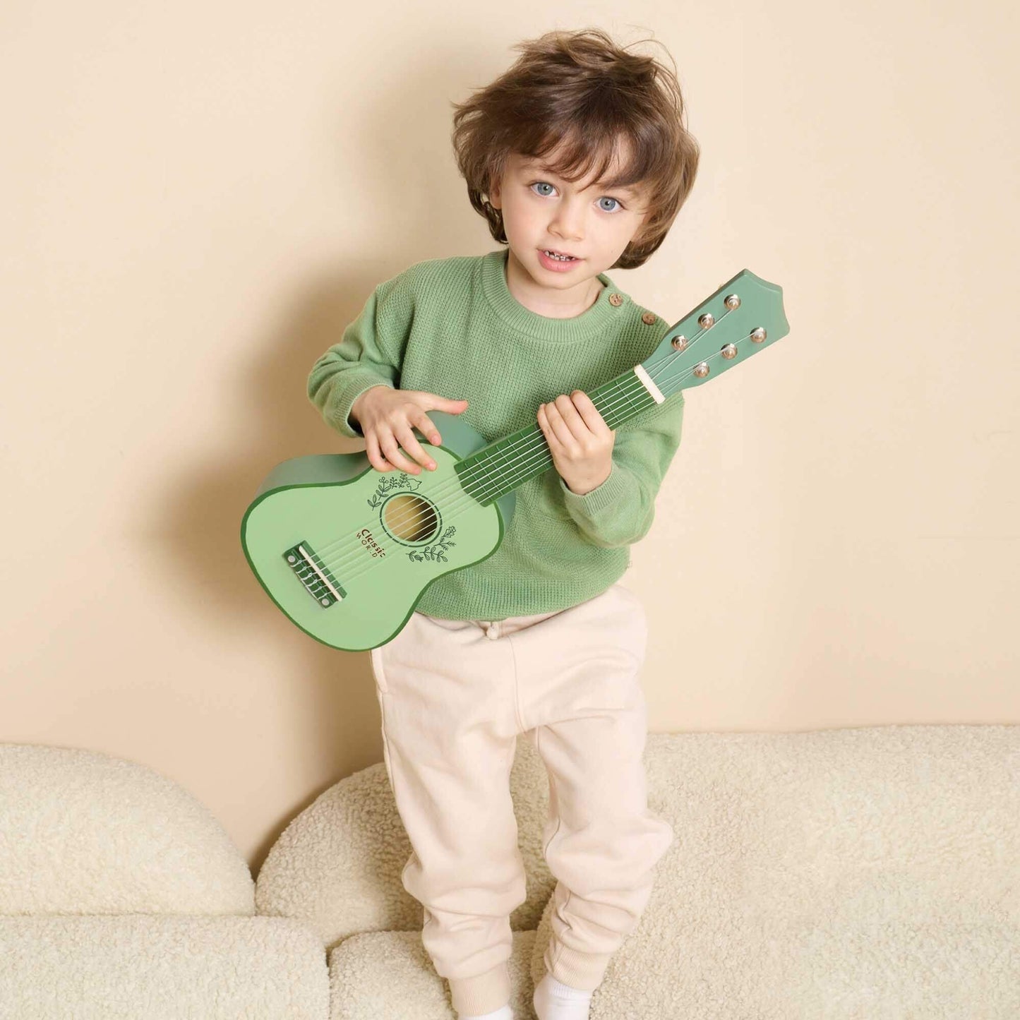 A child playing with a vintage-style wooden toy guitar in green, showcasing its child-friendly size and elegant floral design for early musicians.