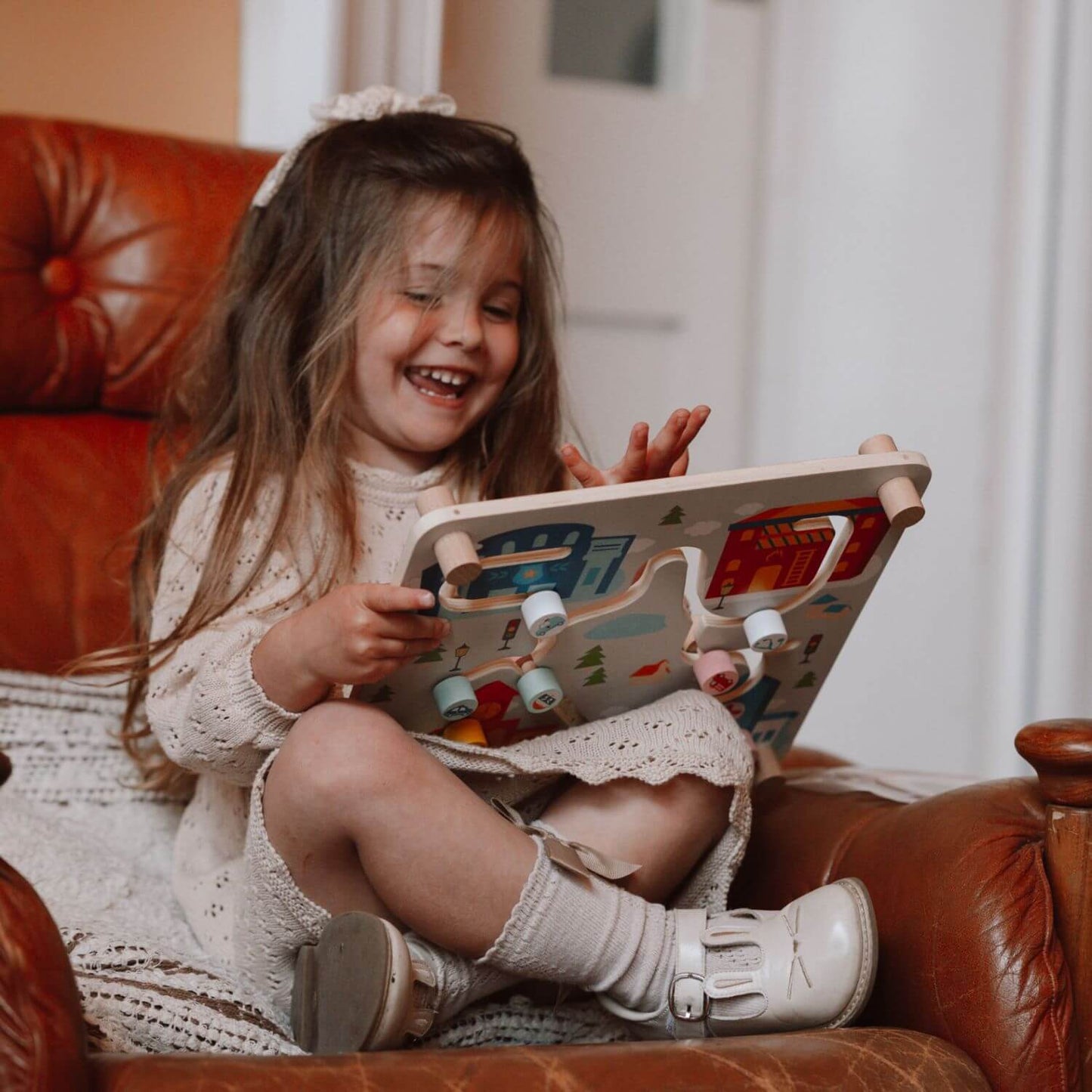 A happy child sitting on a chair, joyfully playing with the Classic World 2-in-1 City Pathfinder, exploring the city-themed side.