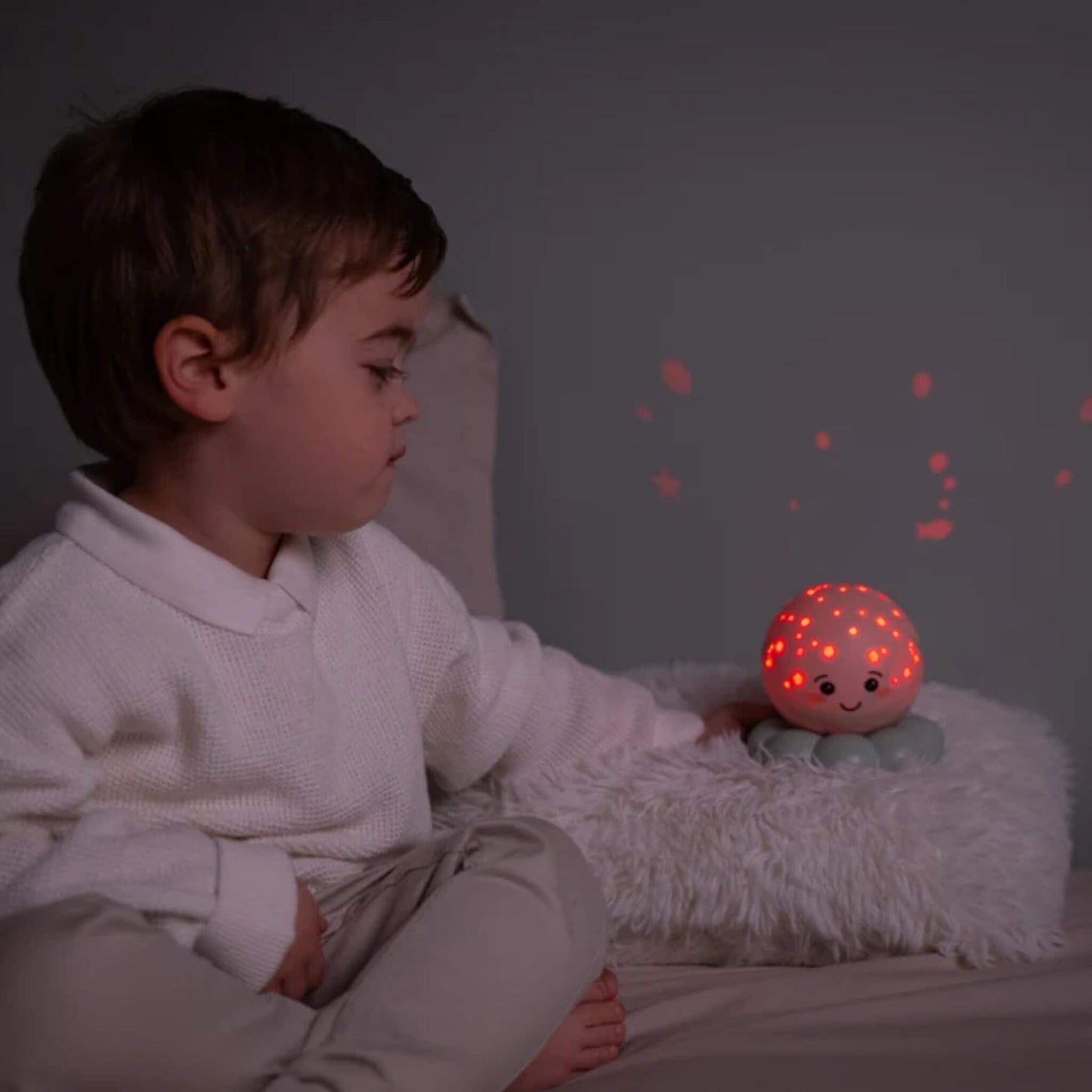 A child watching a glowing octopus night light projecting red shapes onto the bedroom wall.