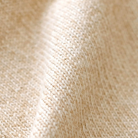 Close-up of soft beige organic cotton knit showing the fine knitted texture and neatly finished edge of a baby comforter.