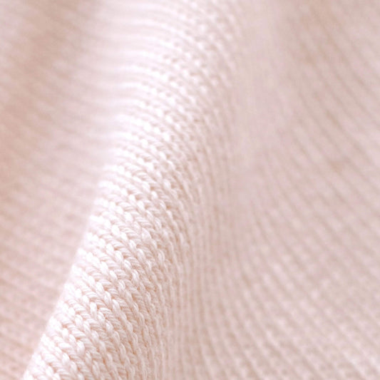 Close-up of soft blush pink organic cotton knit showing the fine knitted texture and neatly finished edge of the baby comforter.
