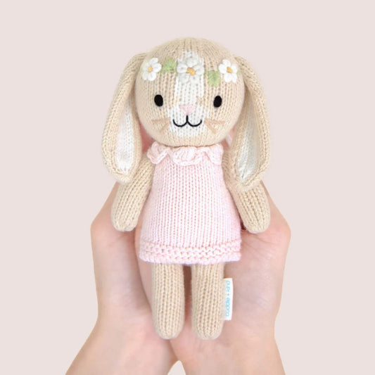 Small knitted bunny doll held in hands showing scale, wearing a soft pink dress with embroidered floral headband.