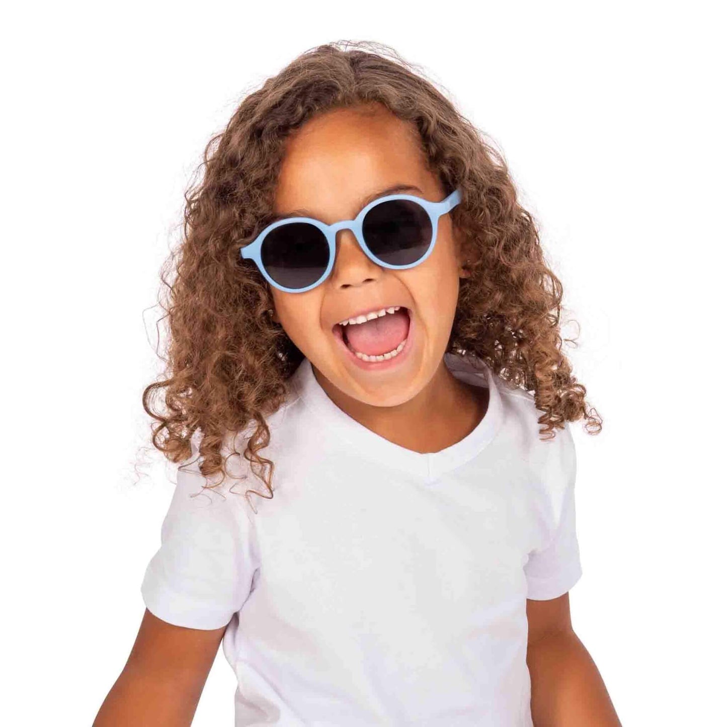 A young child with curly hair wearing blue round sunglasses and a white t-shirt, smiling brightly against a plain background.