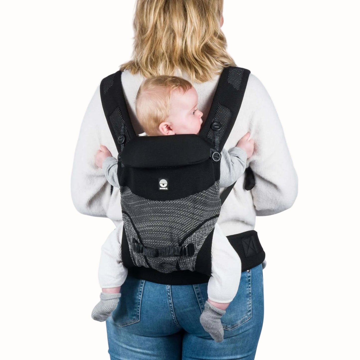 Rear view of a mother carrying a baby on her back in a black baby carrier, showing the back carrying position.
