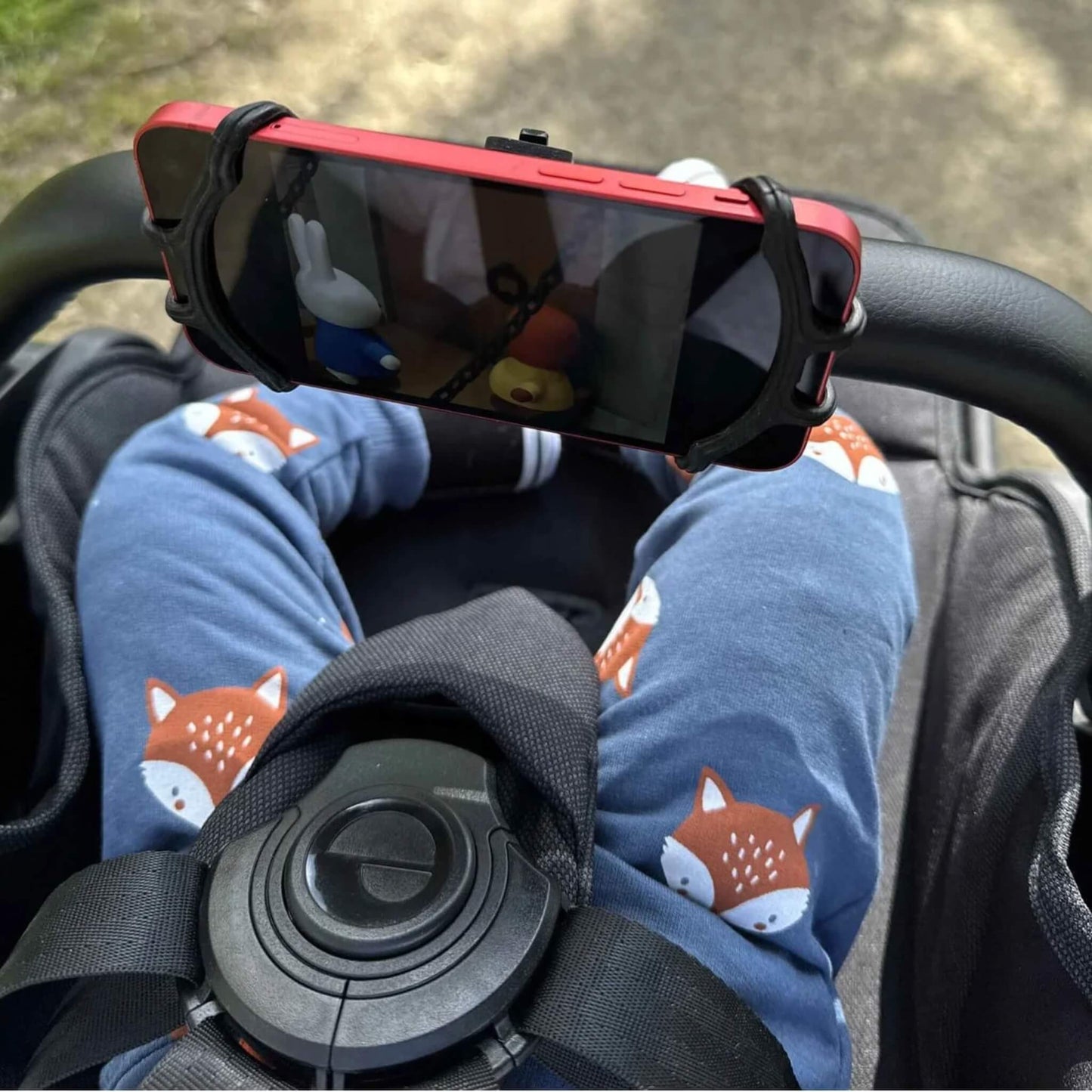 A smartphone secured in a black phone holder on a stroller handlebar, showing a cartoon video on the screen.