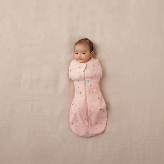 Baby snuggled in a Cocoon Swaddle Bag in a soft pink daisies print, offering a cosy, secure fit for peaceful sleep.