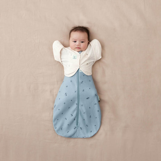Baby wearing a cardigan in oatmeal over a blue sleeping bag. A soft, breathable transition aid for moving from swaddling to arms-out sleep.