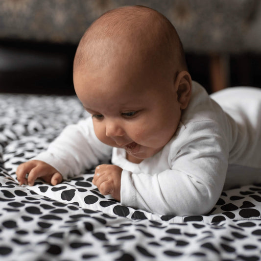 Baby lying on tummy on a padded black and white patterned playmat, focusing closely on the bold high contrast shapes during floor play.