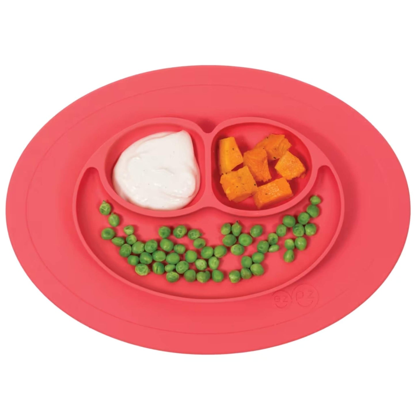 Coral silicone suction placemat with three divided sections containing food including peas, sweet potato and yoghurt.