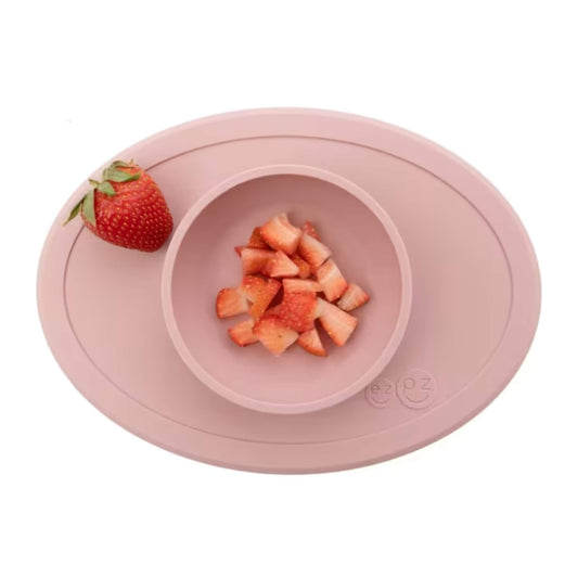 A blush pink silicone toddler bowl with a central raised dish holding neatly chopped strawberry pieces, viewed from above.