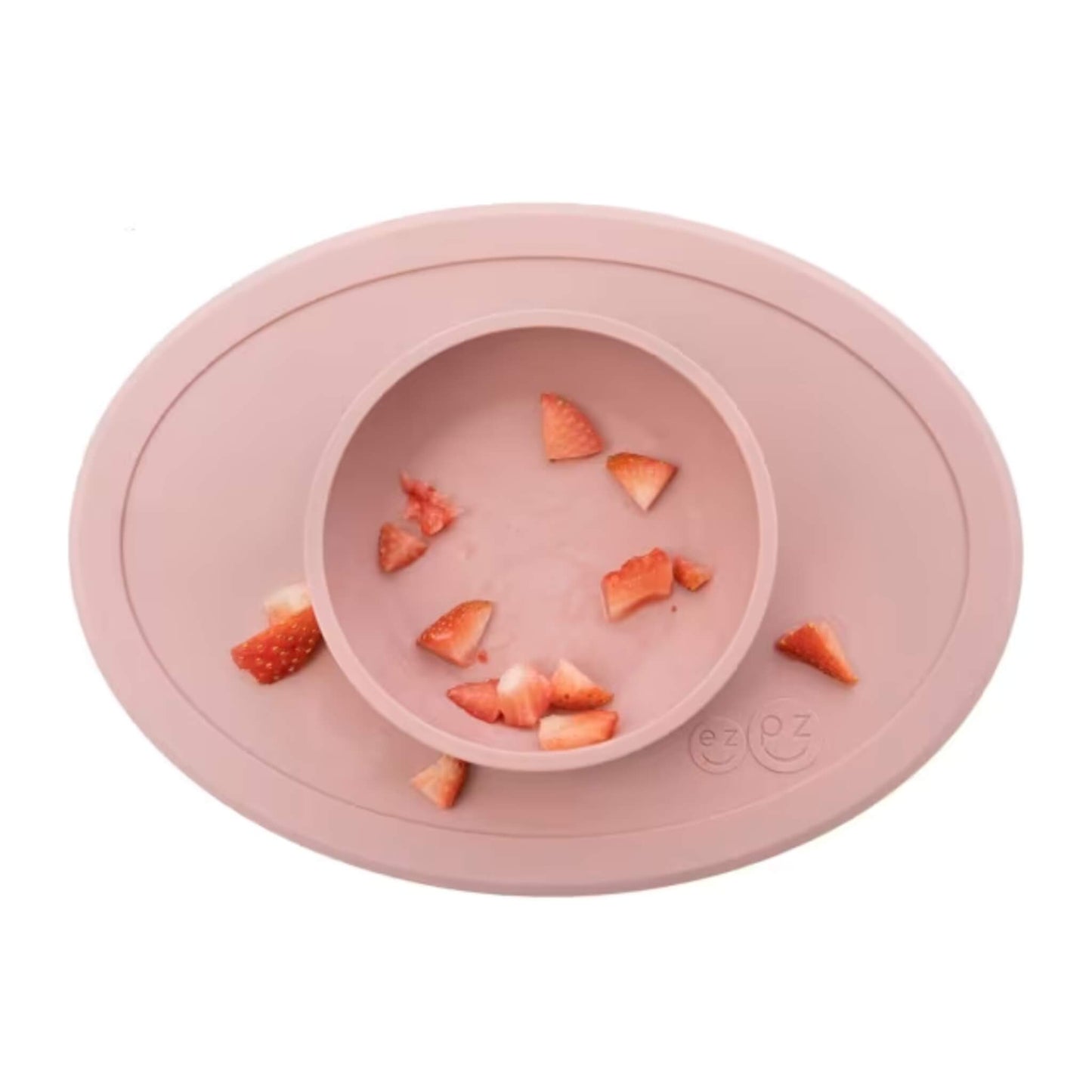 A blush pink silicone toddler bowl with scattered strawberry pieces inside and around a raised central dish, shown from above.