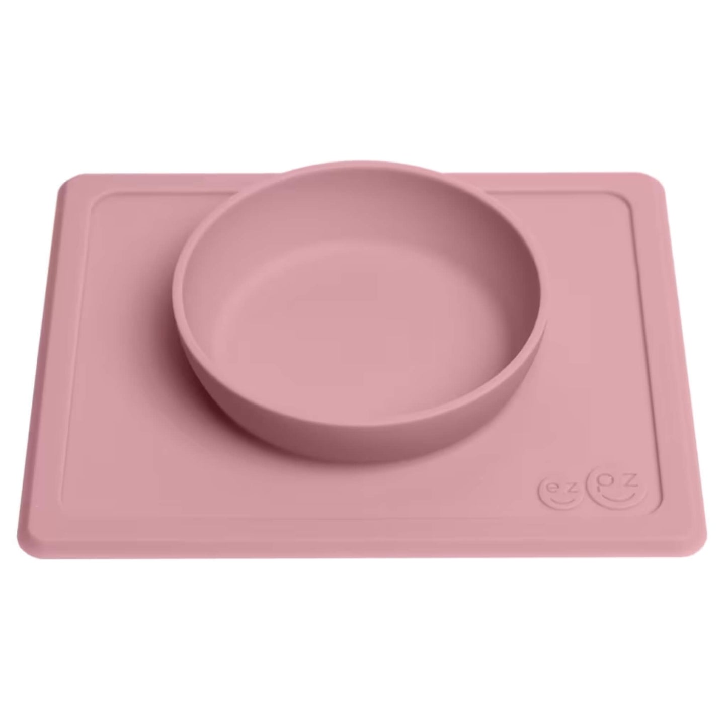 A blush pink silicone baby bowl with integrated placemat shown from an angle, designed to stay in place and make self-feeding easier.