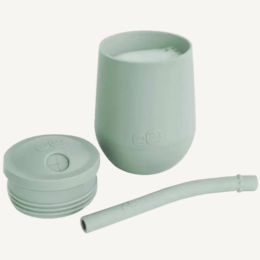 Sage green silicone training cup with matching short straw and lid shown beside it.