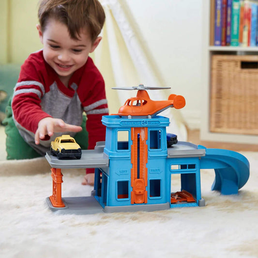 Young child playing on the floor with the Green Toys Parking Garage, pushing the yellow car across the top ramp while smiling.