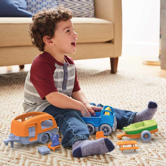 Young child sitting on a cream carpet, happily playing with the RV Camper Set, holding the blue truck with the camper, chairs and characters scattered nearby.