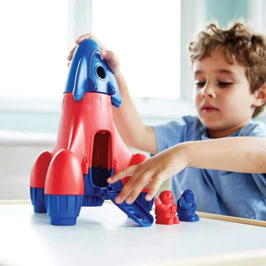 Child playing with the Green Toys Rocket, lifting the nose cone and opening the back hatch with two astronauts nearby.