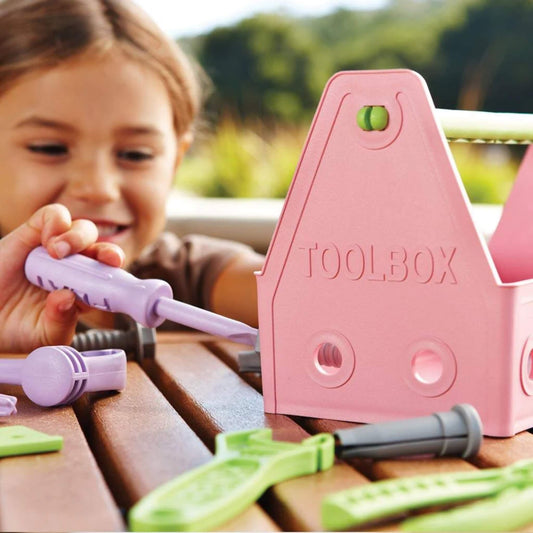 A child using the lilac screwdriver from the Green Toys Tool Set to twist a bolt into the pink toolbox during play.