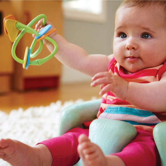 Smiling baby wearing a striped outfit holds the Green Toys Twist Teether with both hands, exploring it while seated on a soft surface.