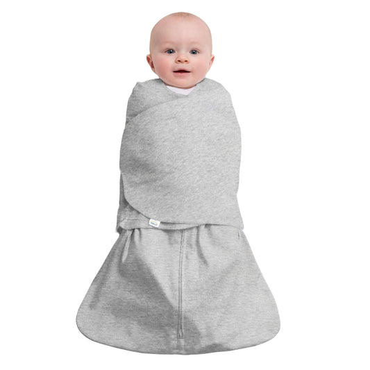 Baby wearing HALO SleepSack Swaddle in heather grey, arms tucked in, showing snug fit and soft cotton fabric for safer sleep.