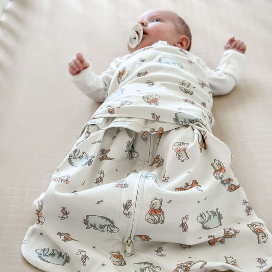 Baby sleeping peacefully in Halo Sleepsack Swaddle featuring Winnie the Pooh and friends print. Provides warmth, comfort, and secure swaddling.
